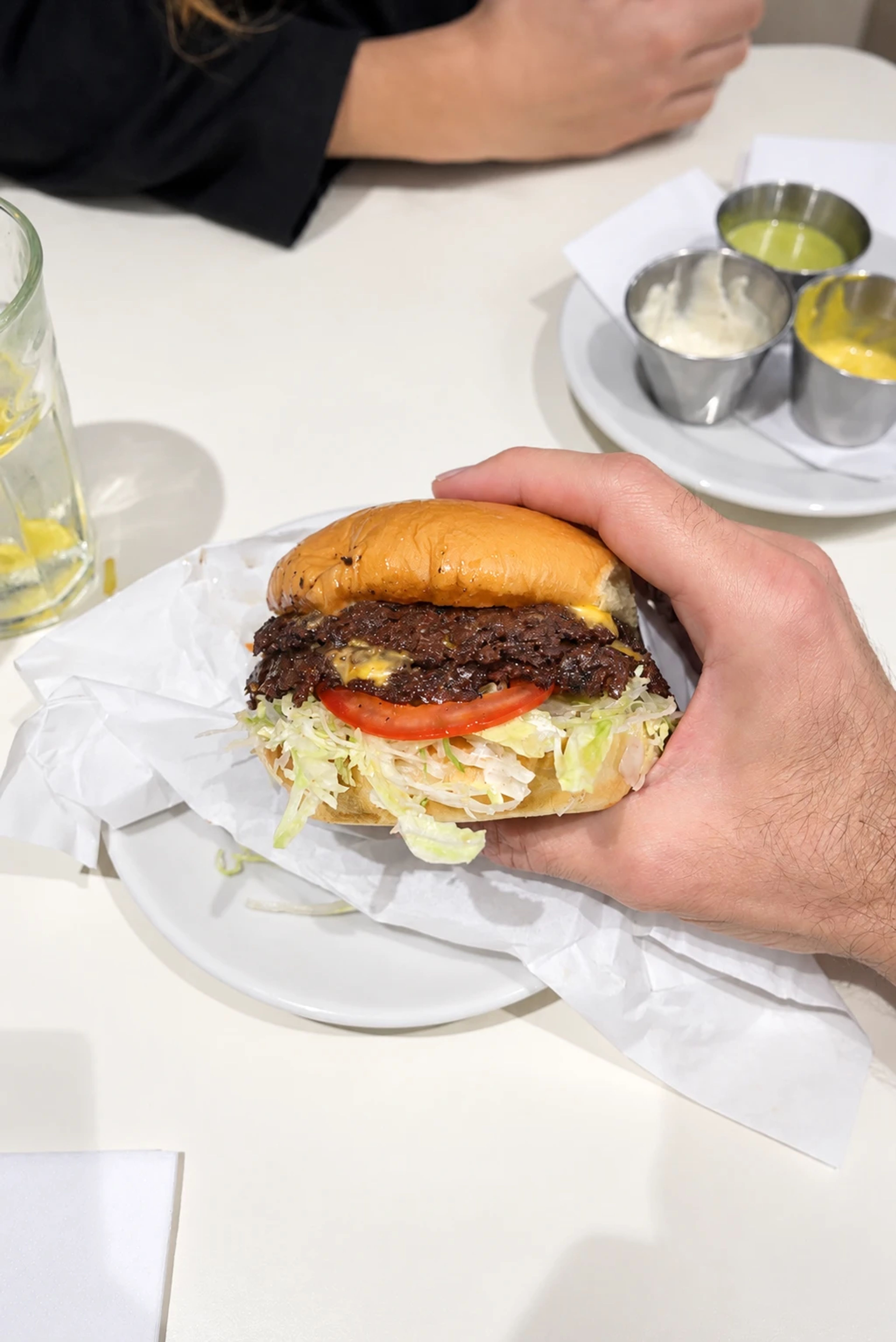 Hand hält einen Double-Burger mit zwei Smash-Patties, Käse, Tomate und Salat