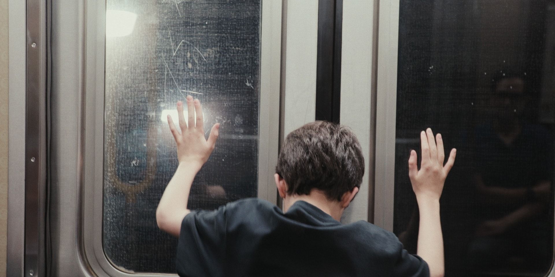 A boy presses both hands to the window of a subway car door.