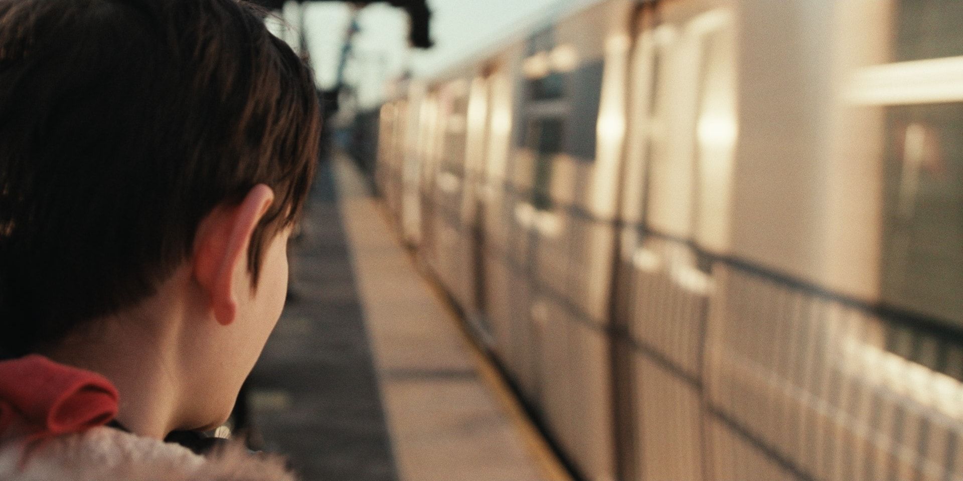 A boy on an elevated platform watches a silver train come in.