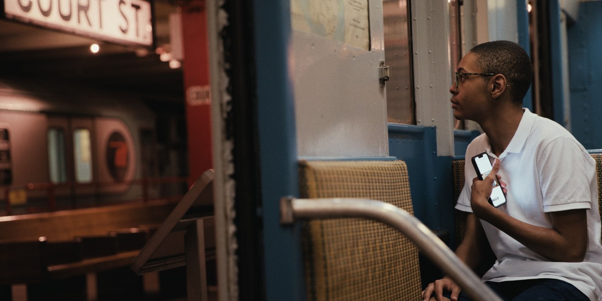 A young man holds his phone to his chest aboard a vintage subway car at the New York Transit Museum.