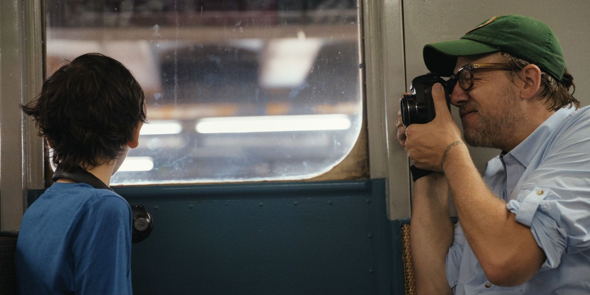 A boy looks out of a subway car window while a photographer takes his picture.