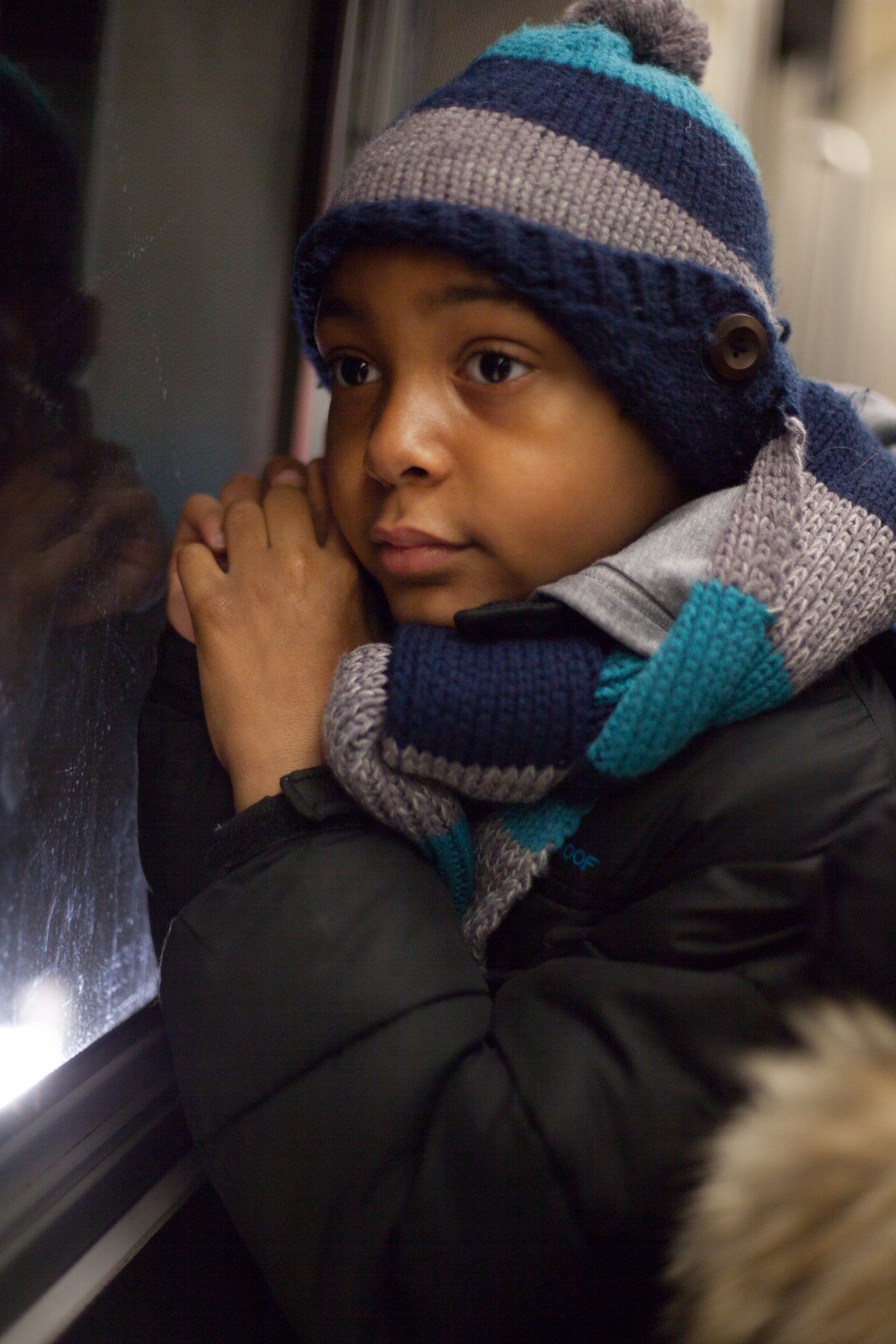 Mason, in a striped knitted hat and scarf, leans against a subway car window.