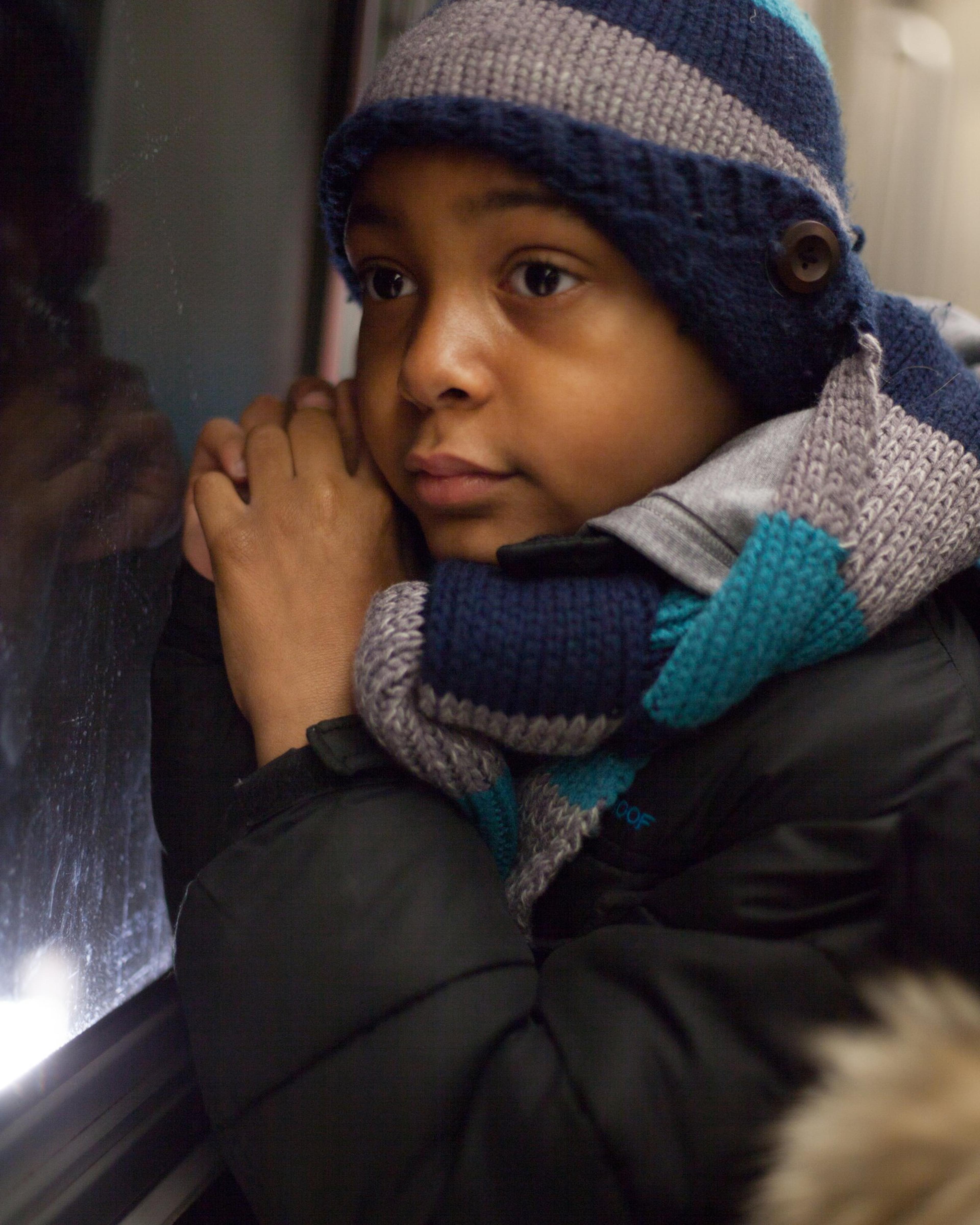 Mason, in a striped knitted hat and scarf, leans against a subway car window.