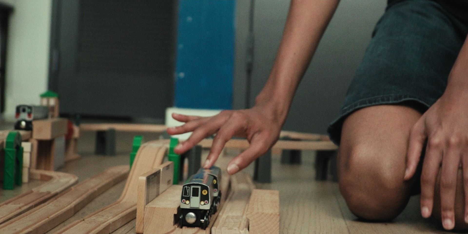 A hand guides a toy subway train along a wooden track.