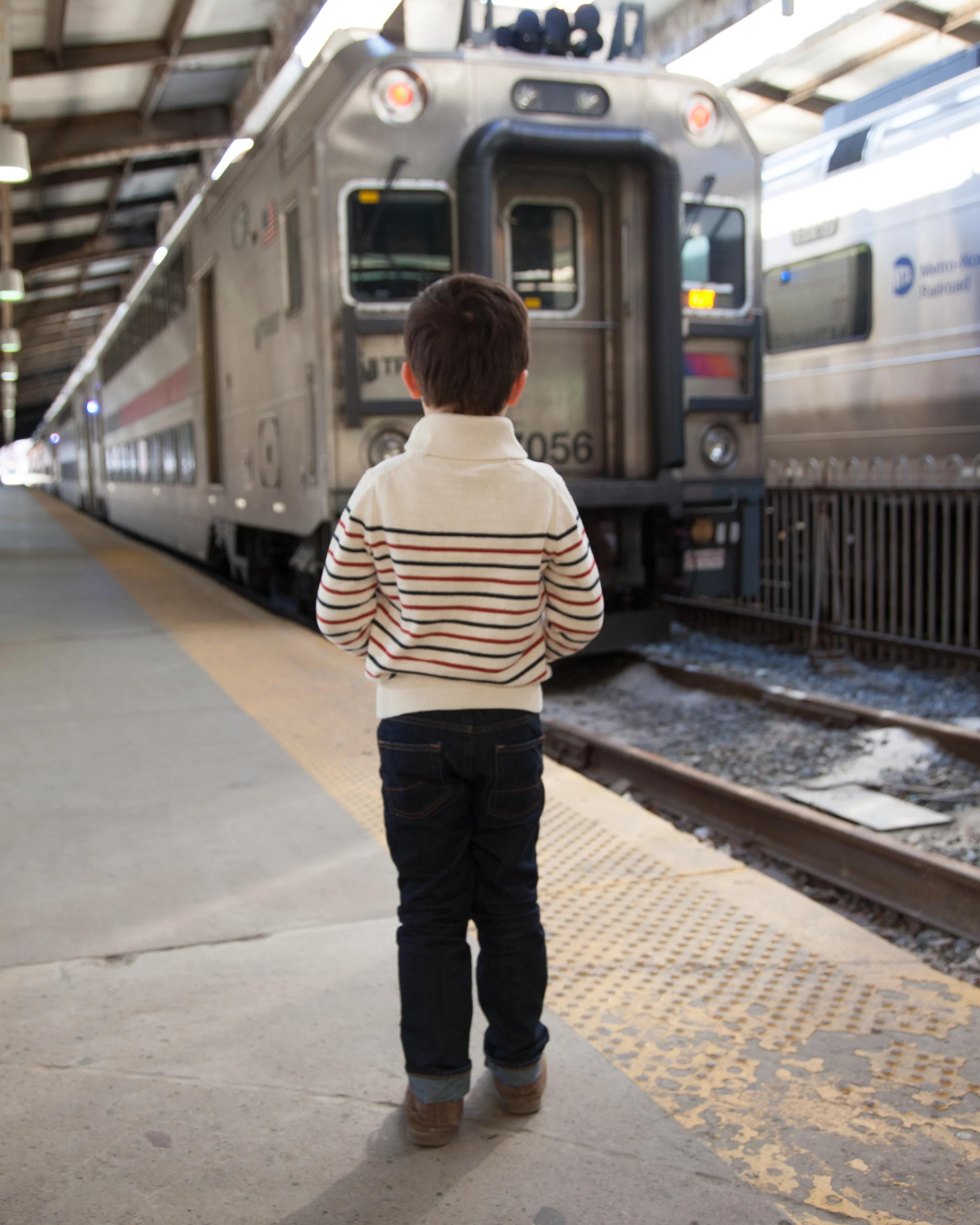A boy in a striped sweater watches a commuter train from the platform, seen from behind.