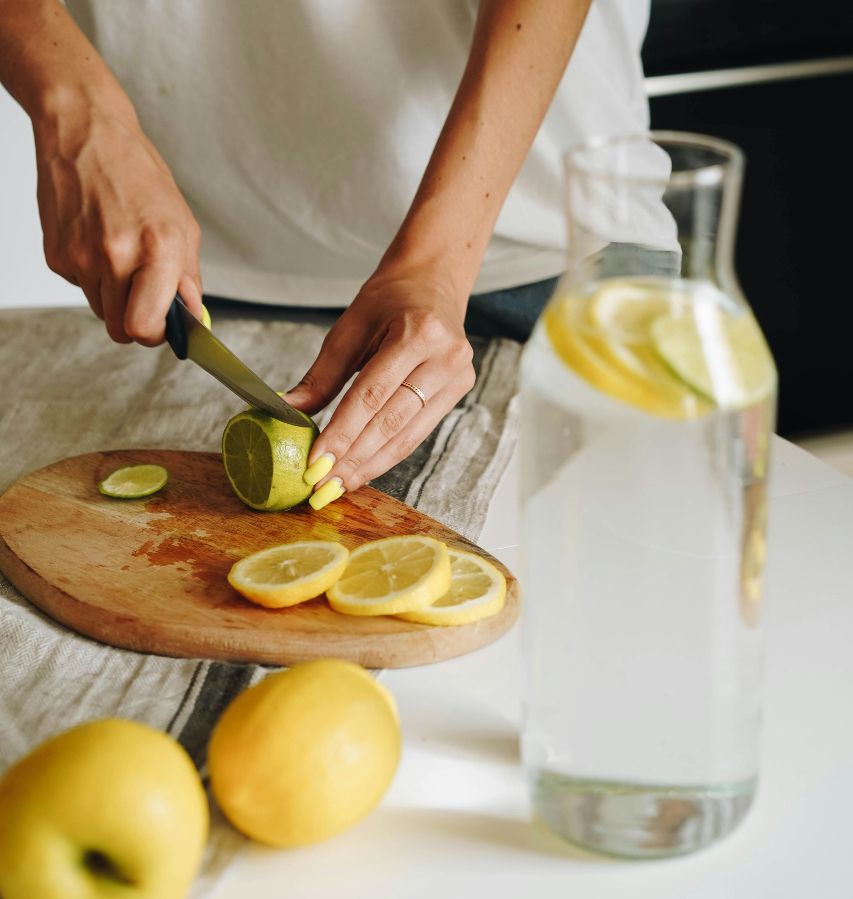 A person slices lemons behind a carafe of water.