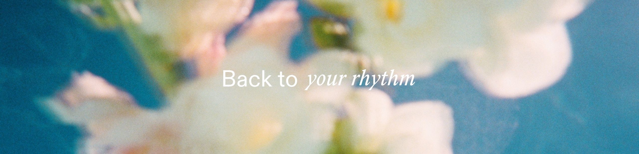 Een vrouw zit met een kopje thee voor de bank en aait haar hond.