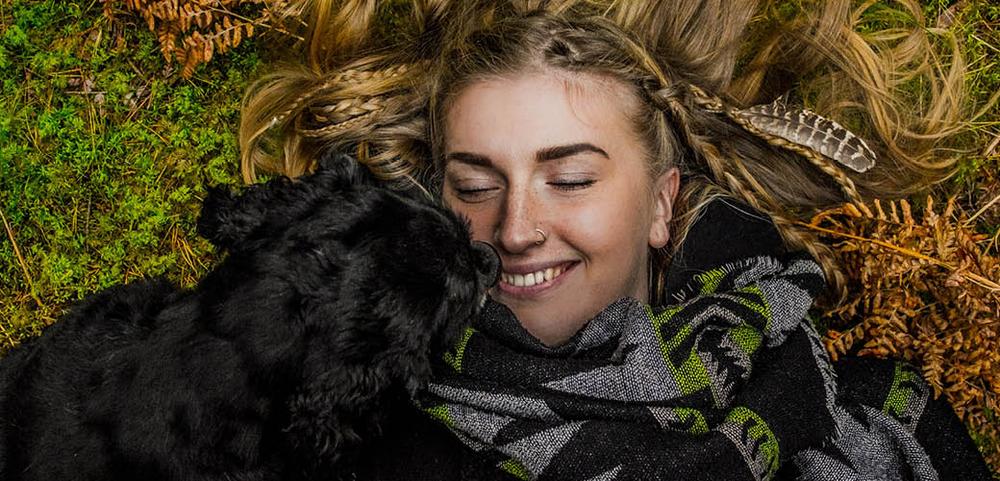 a woman is laying on the ground with a black dog . a woman is laying on the ground with a black dog .