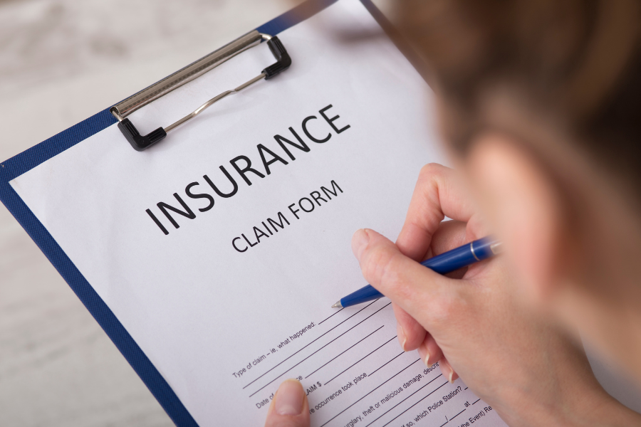 A person's hand filling out an insurance claim form with a blue pen.