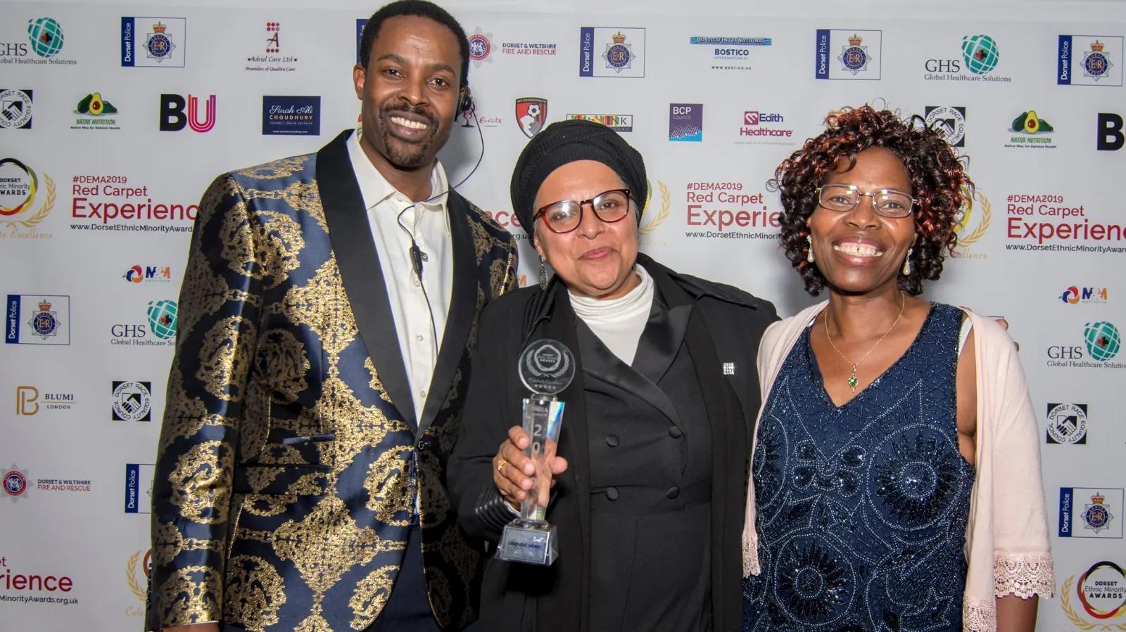 A winner holding a crystal trophy with two guests