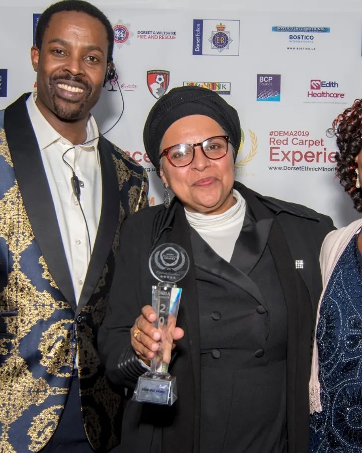 A winner holding a crystal trophy with two guests
