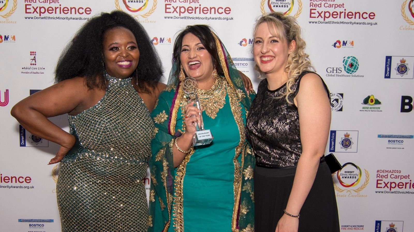 Three guests smiling together in front of the sponsor backdrop