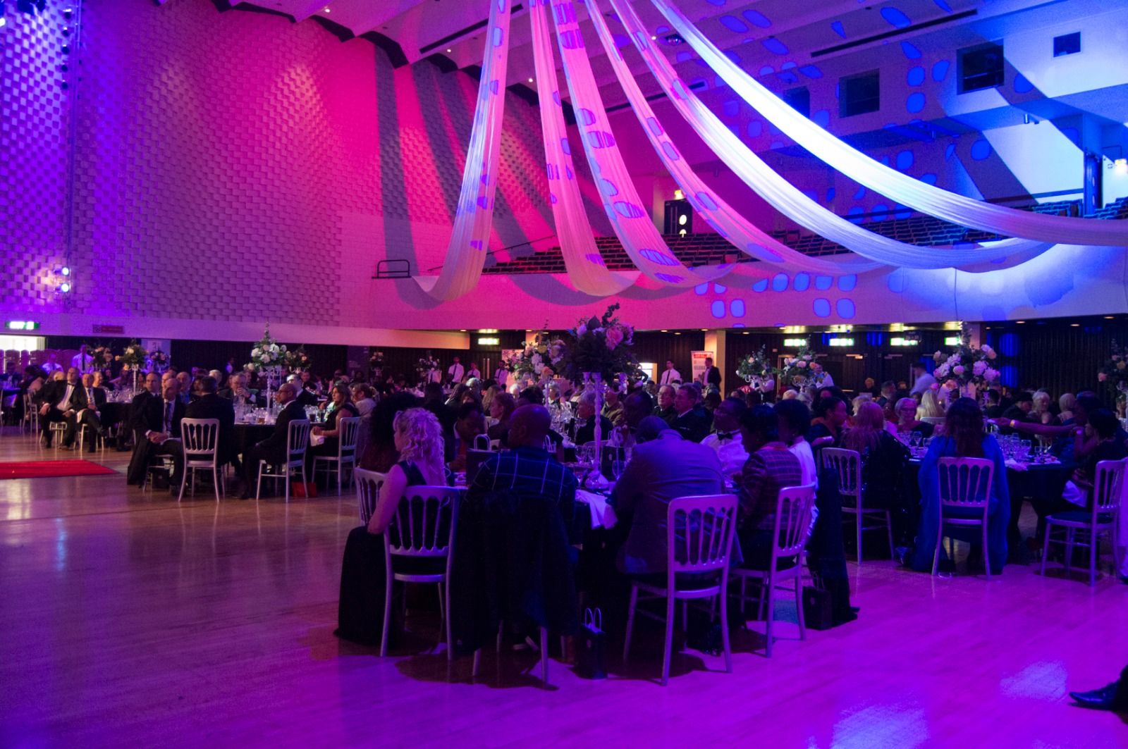 The ballroom full of guests at dinner tables under draped ceiling lights