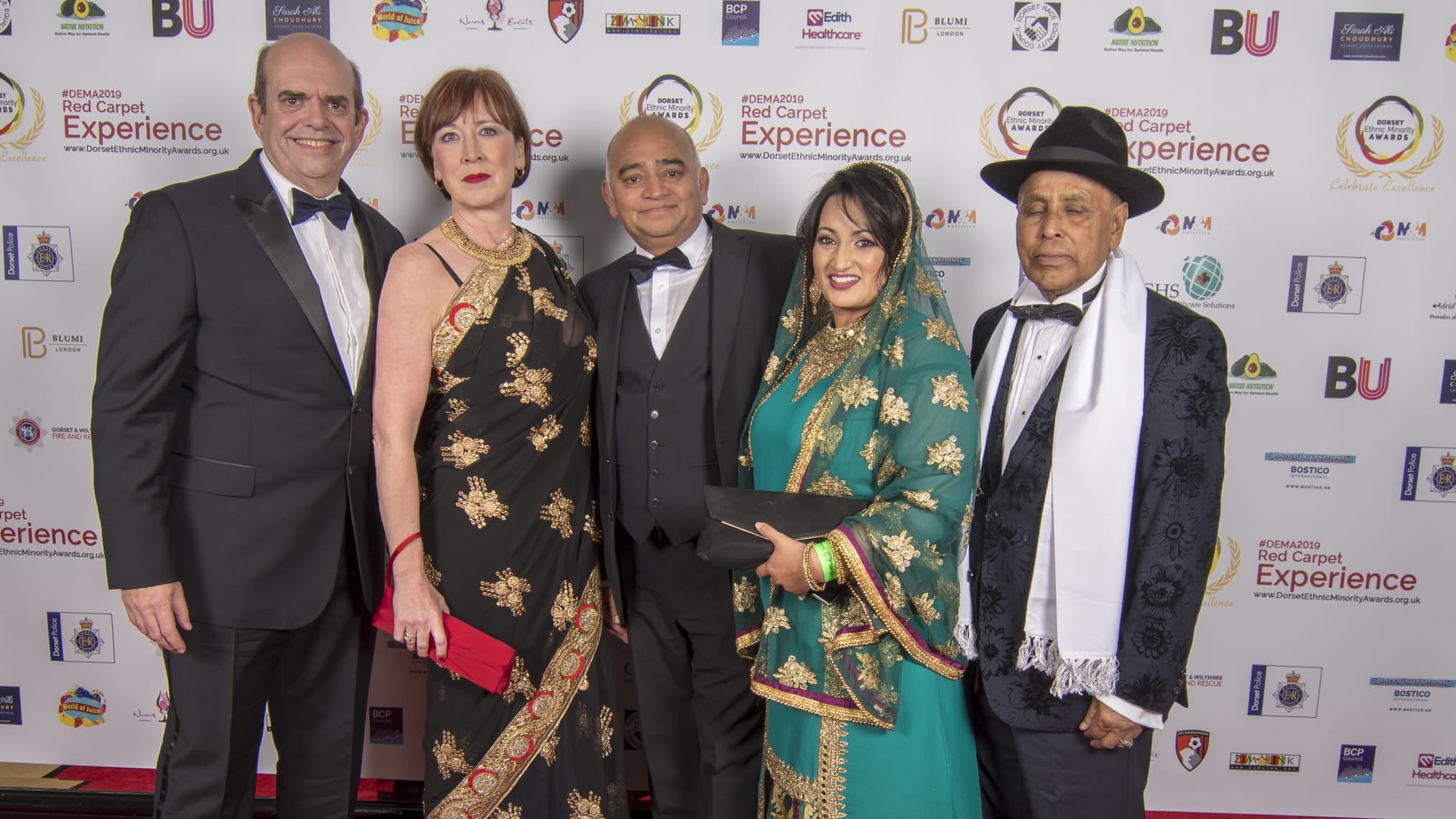 A group of guests in formal and traditional dress on the red carpet