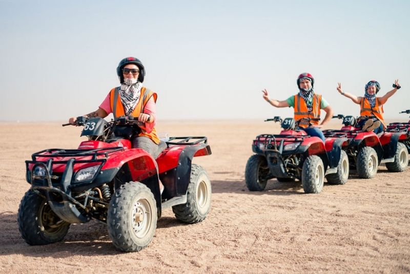 Uczestnicy w kaskach i kamizelkach na czerwonych quadach na pustyni podczas safari z Marsa Alam