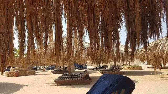Cień pod parasolem z suchych liści palmowych na plaży Sharm el Naga z drewnianymi leżakami na piasku