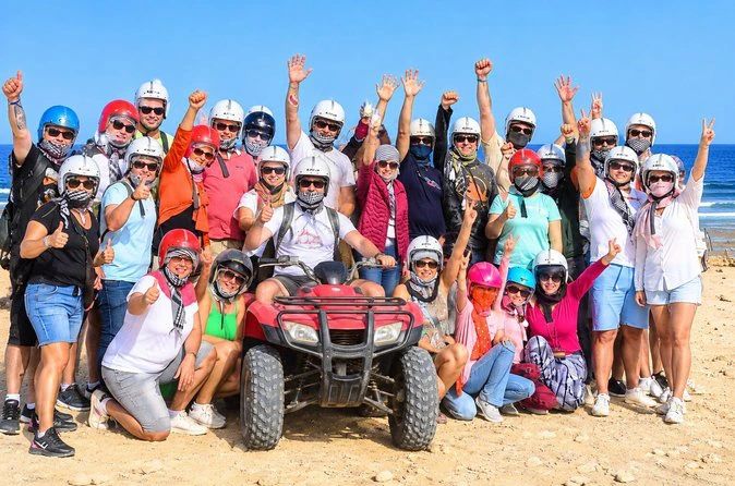 Grupa uczestników w kaskach wokół czerwonego quada, w tle wybrzeże Morza Czerwonego, podczas quad safari z Marsa Alam