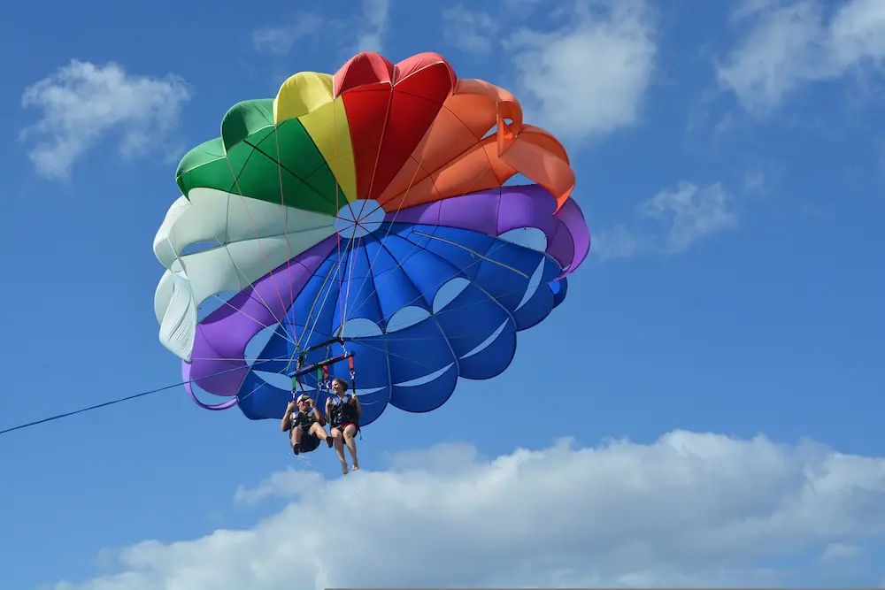 Para uczestników parasailingu pod kolorowym, tęczowym spadochronem holowanym na linie