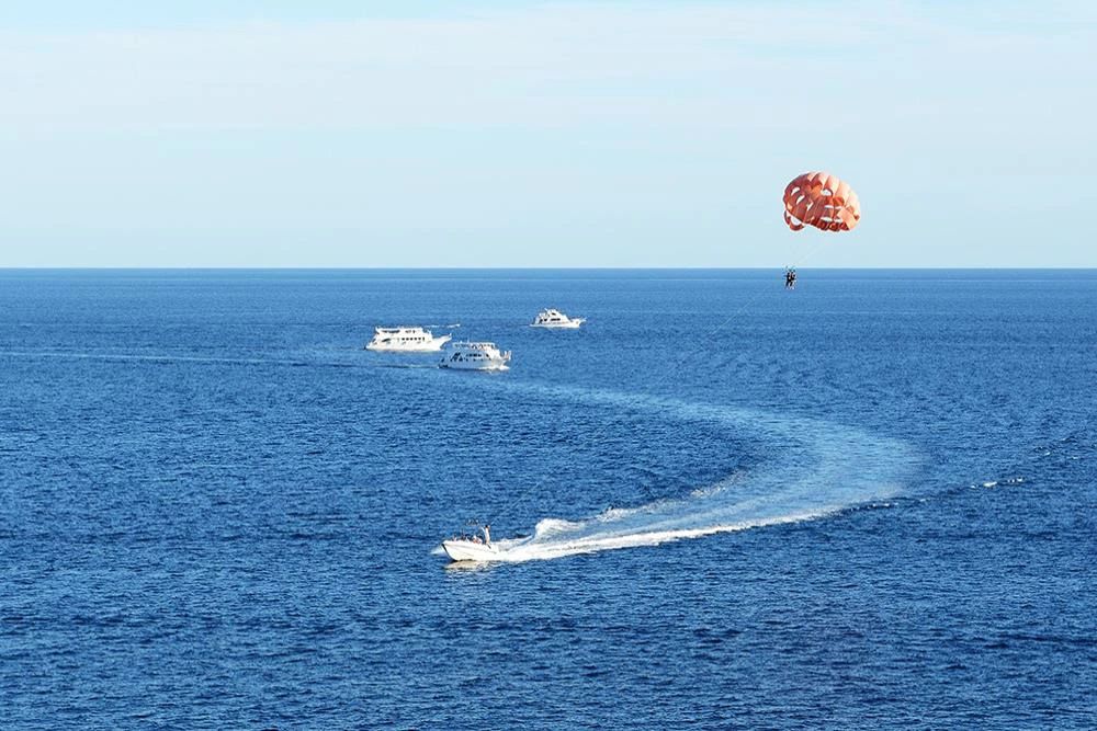 Lot na parasailingu za motorówką nad Morzem Czerwonym - spadochron w powietrzu i kilwater łodzi, w tle inne łodzie