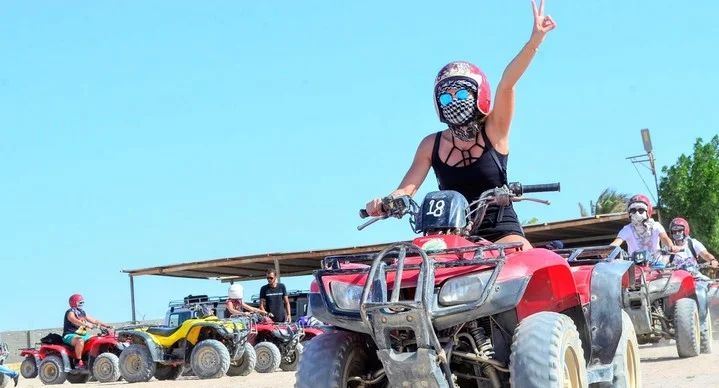 Uczestniczka na czerwonym quadzie w kasku i chuście, quady ustawione w bazie na pustyni podczas Quad Safari 5h z Marsa Alam