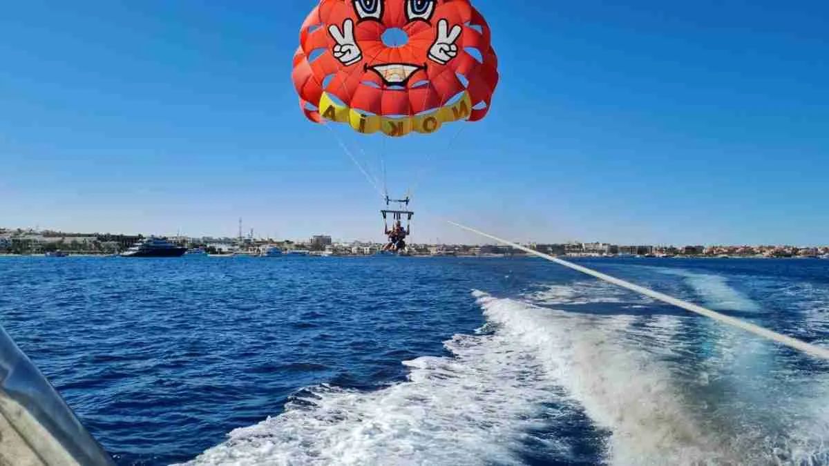 Spadochron parasailingowy unoszący uczestników nad Hurghadą - w tle panorama miasta, Morze Czerwone i kilwater motorówki