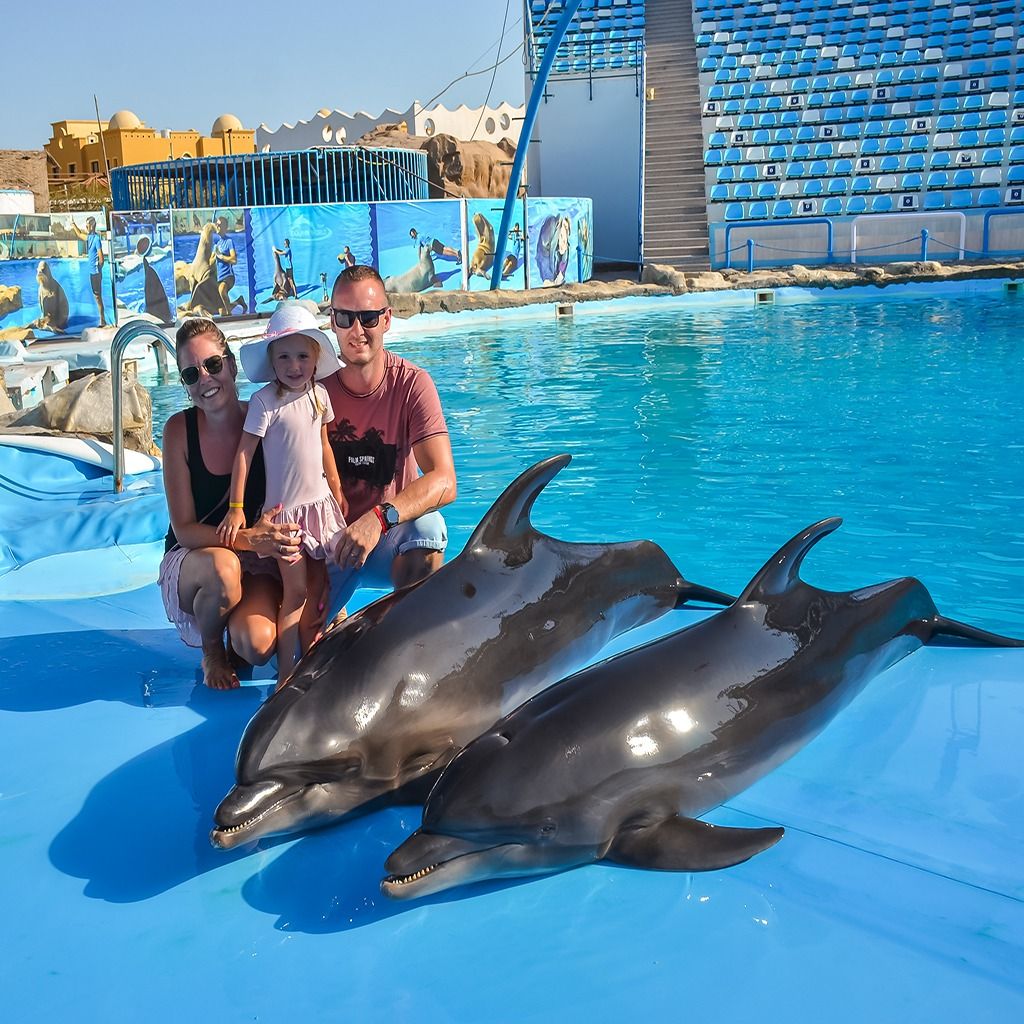 Rodzina z dzieckiem pozująca z dwoma delfinami przy basenie delfinarium
