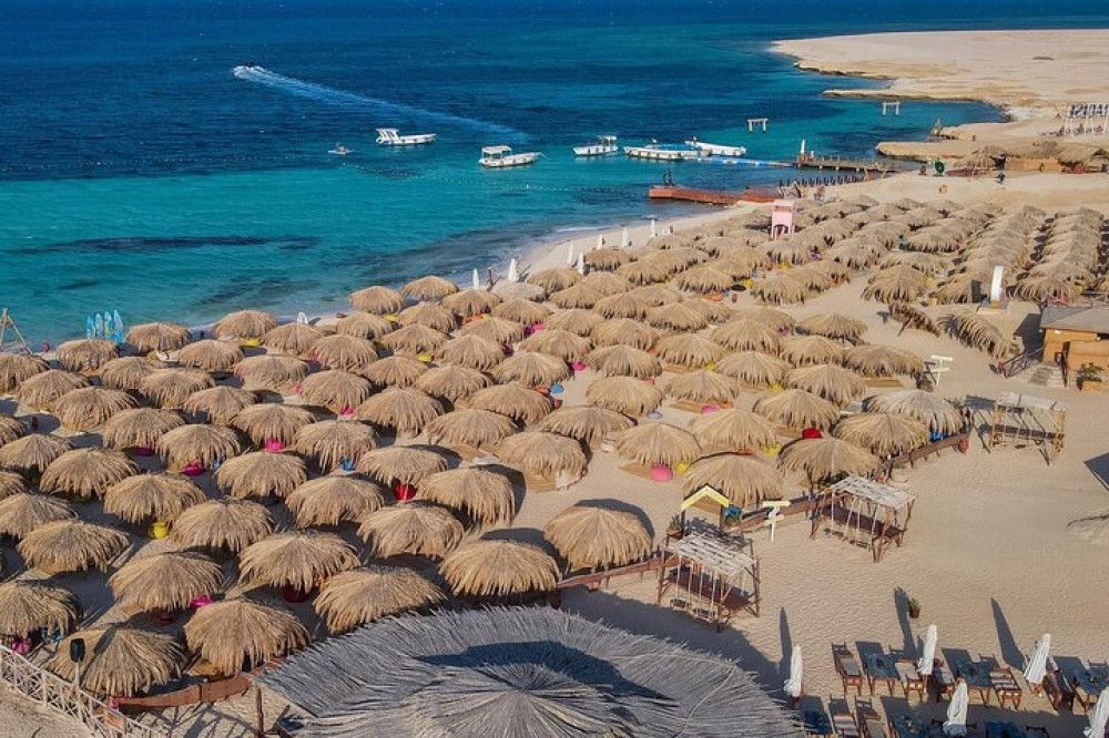 Widok z góry na plażę Hula Hula z rzędami krytych strzechą parasoli, białym piaskiem i turkusową laguną Morza Czerwonego