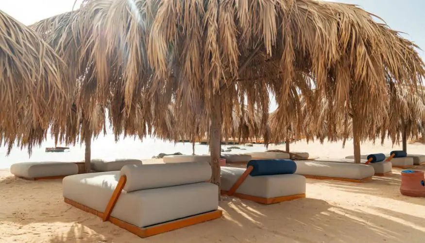 Wygodne materacowe leżanki pod parasolami z liści palmowych na białym piasku plaży Ozirea