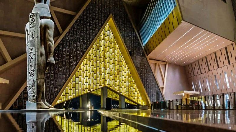 Wnętrze Wielkiego Muzeum Egipskiego (GEM) z monumentalnym posągiem i rozświetloną ścianą podczas wycieczki z Sharm el Sheikh do Kairu