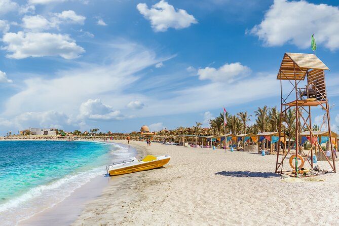 Piaszczysta plaża Abu Dabbab z turkusową wodą, wieżą ratownika, łódką i parasolami w słoneczny dzień
