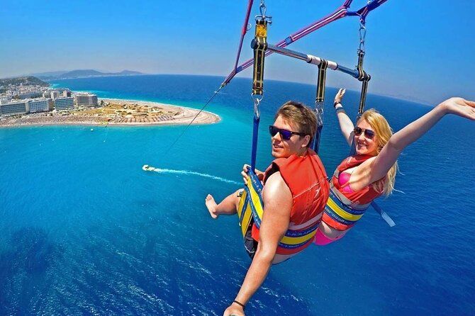 Para lecąca tandemowo na spadochronie parasailingowym wysoko nad turkusową wodą i wybrzeżem