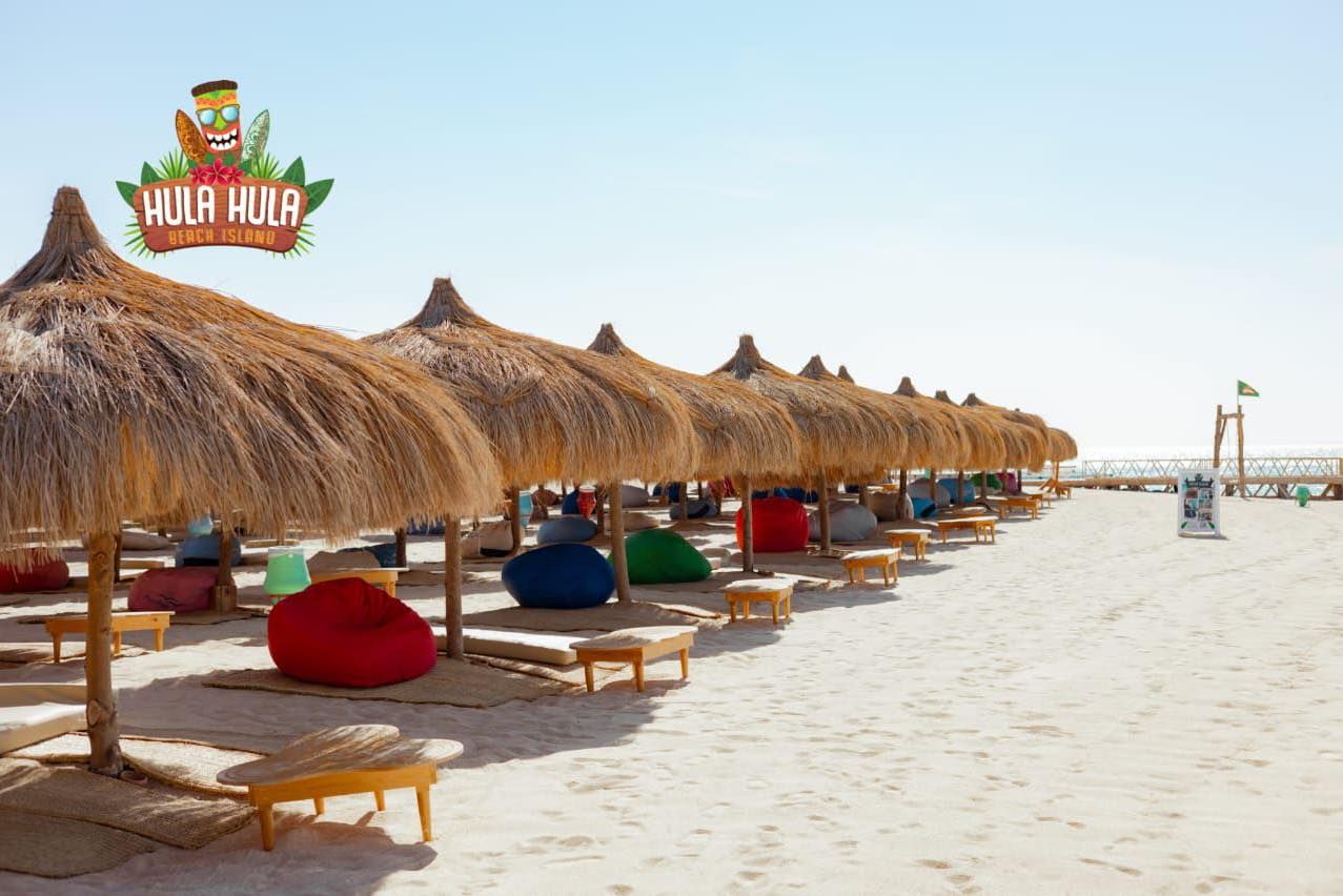 Rząd słomianych parasoli i kolorowych pufów na białym piasku plaży Hula Hula