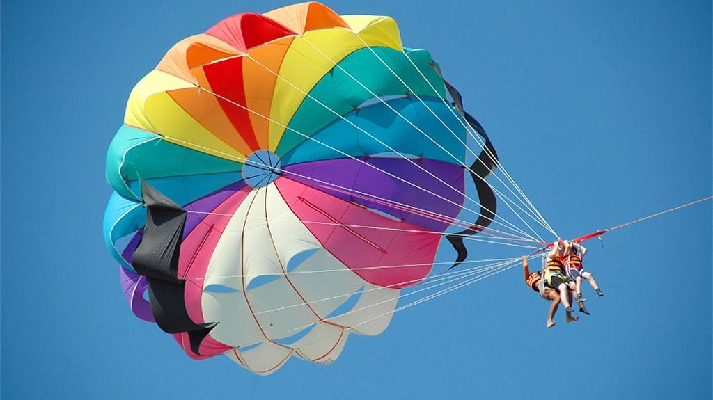 Dwie osoby podczas tandemowego lotu parasailing pod kolorowym spadochronem na tle błękitnego nieba