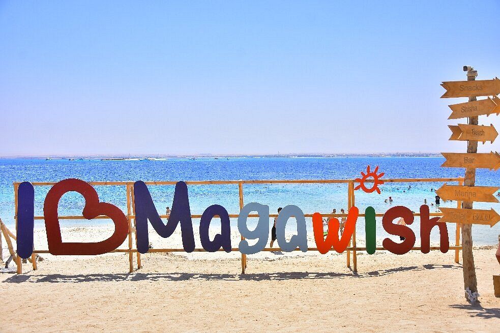 Kolorowy napis I love Magawish na białej plaży wyspy z płytką turkusową wodą Morza Czerwonego i drewnianym drogowskazem