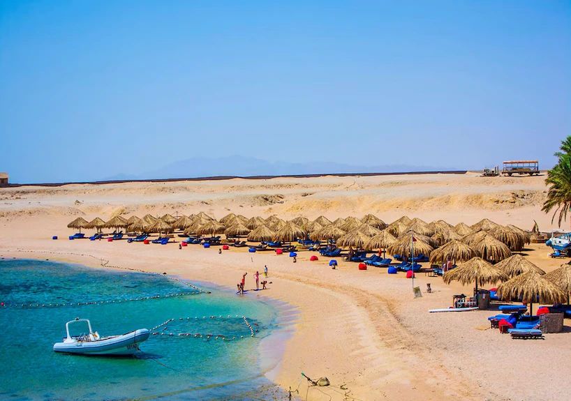 Turkusowa zatoka Sharm el Naga z piaszczystą plażą, parasolami z liści palmowych i łódką - miejsce snorkelingu na wycieczce z Hurghady