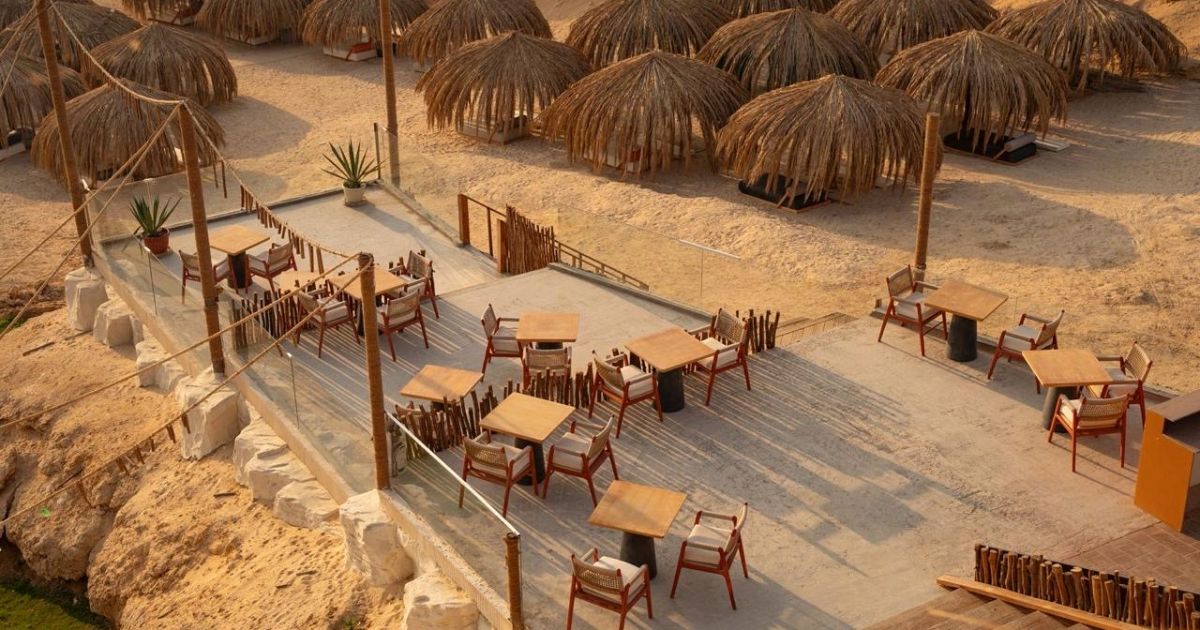 Widok z góry na plażę Ozirea ze słomianymi parasolami, drewnianymi stolikami i leżakami na jasnym piasku