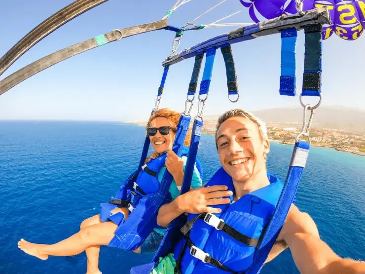 Dwoje uczestników parasailingu w kamizelkach asekuracyjnych podczas wspólnego lotu nad morzem