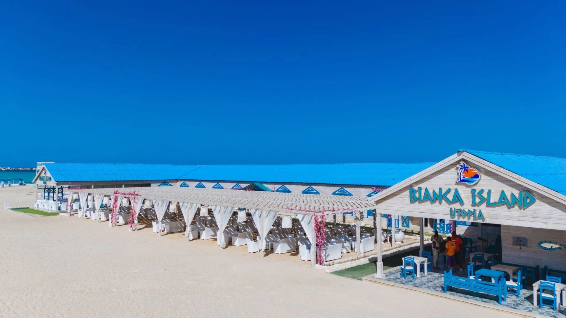 Klub plażowy Bianca Island Utopia koło Hurghady - drewniana altana z rzędami białych stołów pod błękitnym dachem na białej piaszczystej plaży nad Morzem Czerwonym