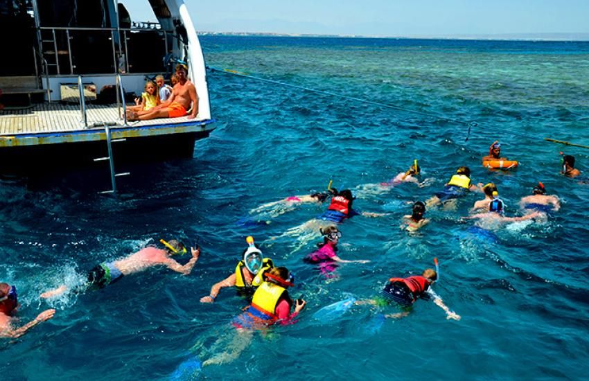 Grupa uczestników w kamizelkach ratunkowych snorkeluje przy łodzi podczas postoju na rafie koło Hurghady