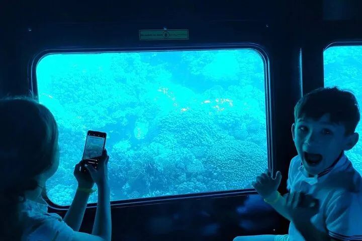 Dzieci oglądające i fotografujące rafę koralową przez okno podwodnego pokładu łodzi Seascope
