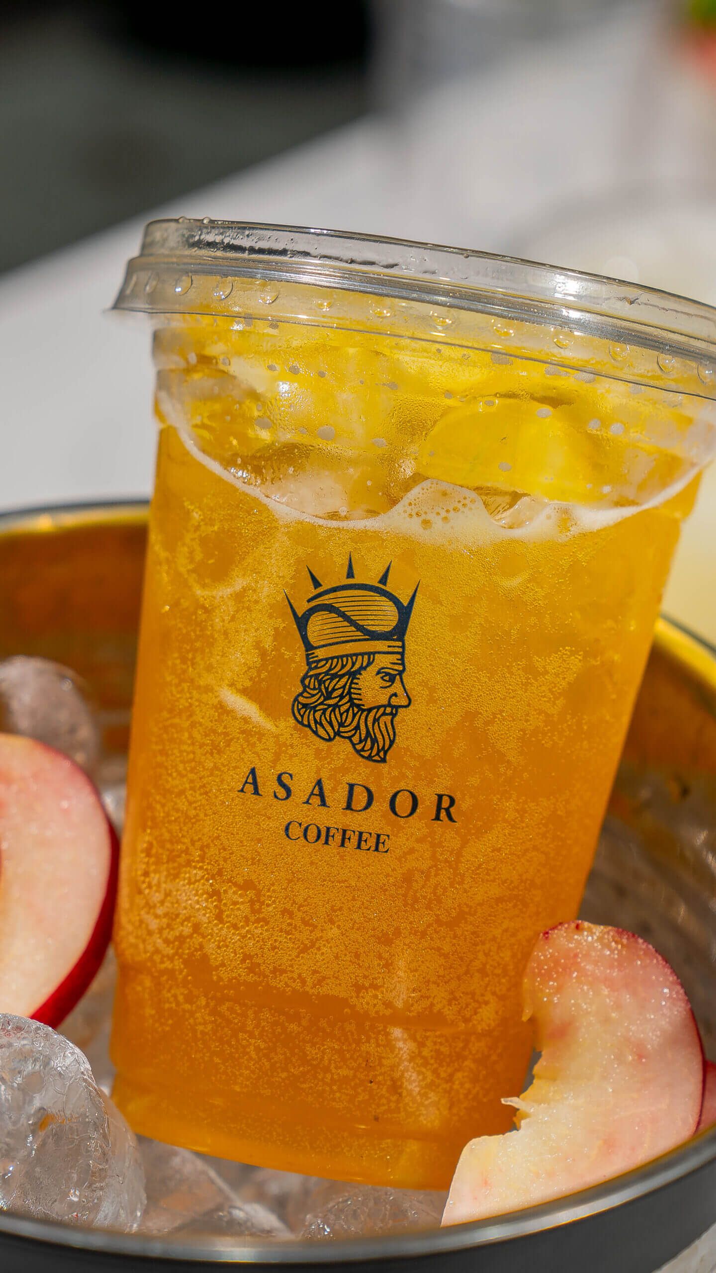 Iced Peach Energy Drink with Fresh Fruit Garnish in Plastic Cup at Asador Coffee El Jadida