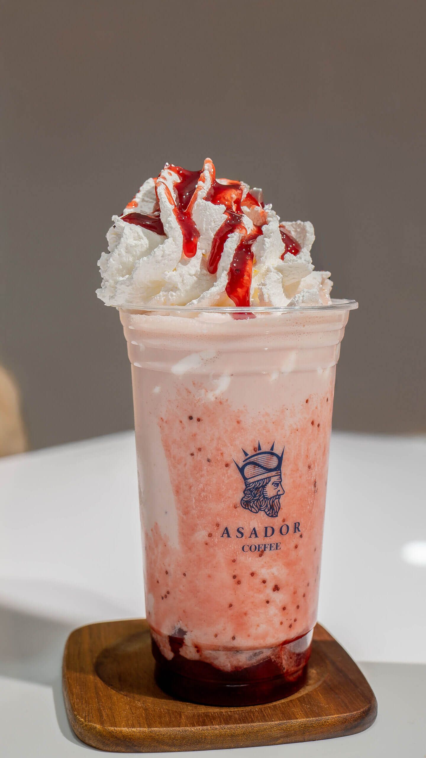 Classic Iced Strawberry Milkshake with Whipped Cream and Red Syrup Drizzle in Plastic Cup at Asador Coffee El Jadida