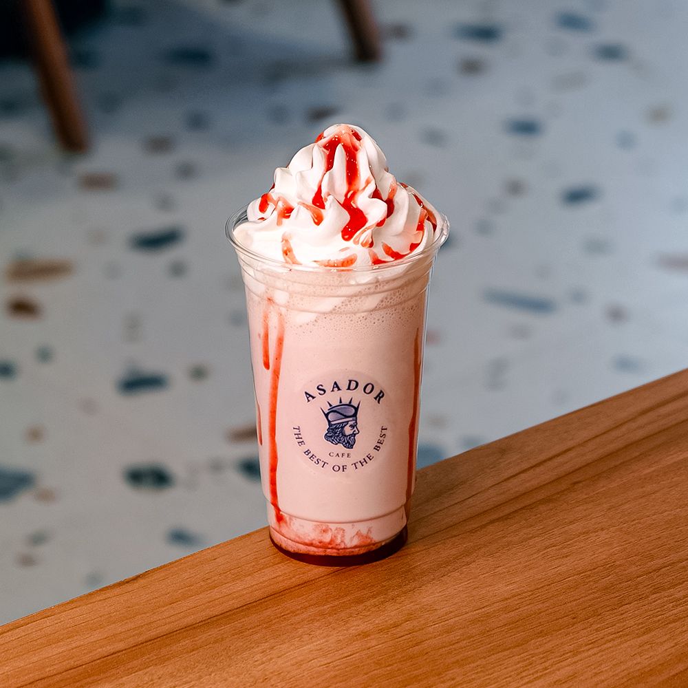 Classic Iced Strawberry Milkshake with Whipped Cream and Red Syrup Drizzle in Plastic Cup at Asador Coffee El Jadida