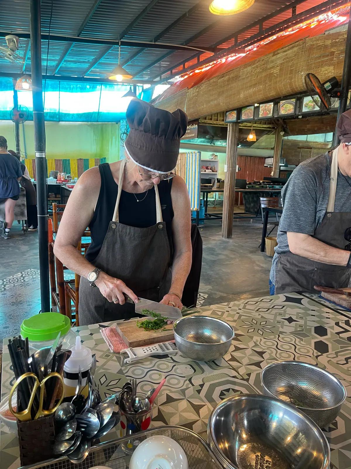 A guest in apron and chef hat preparing ingredients at the cooking class
