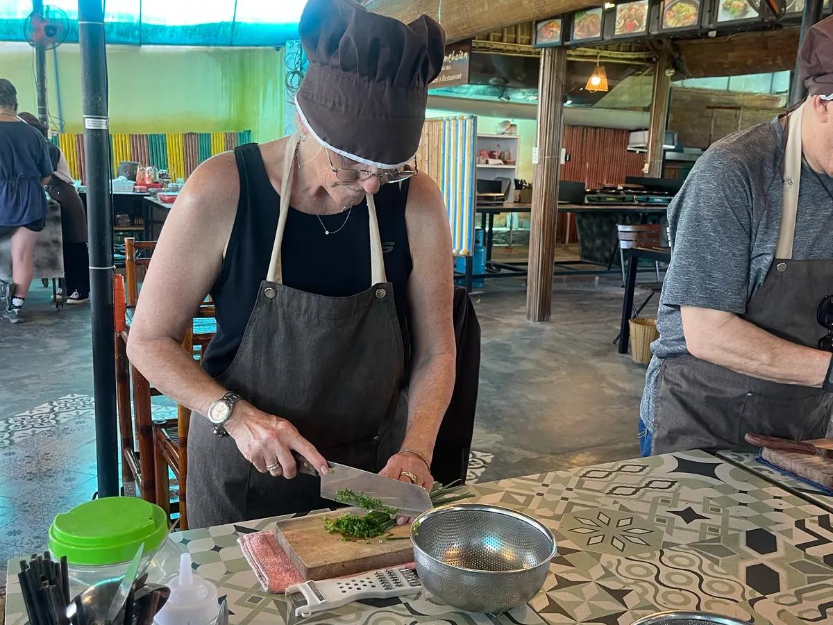 A guest in apron and chef hat preparing ingredients at the cooking class