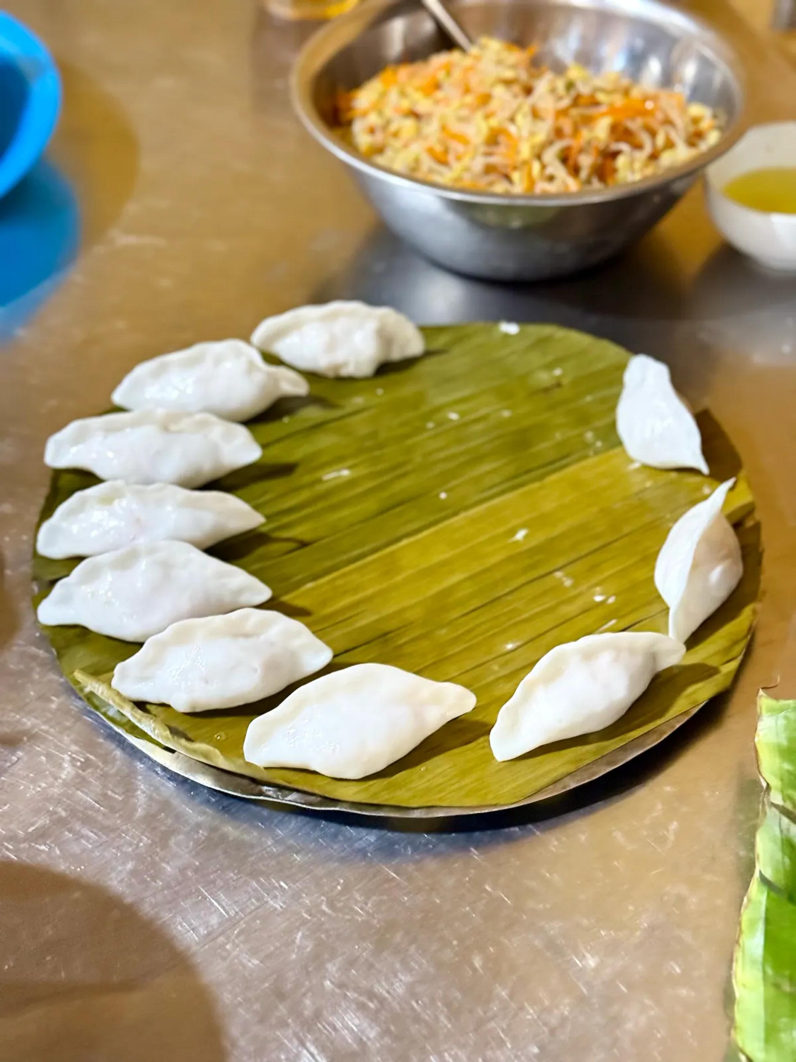 White rose dumplings arranged on a banana leaf beside a bowl of fried shallots