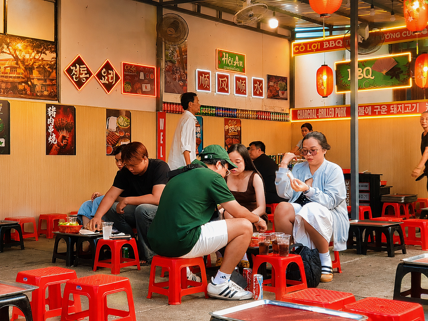 Diners on low red plastic stools at Thịt Nướng Cô Lợi in Hoi An