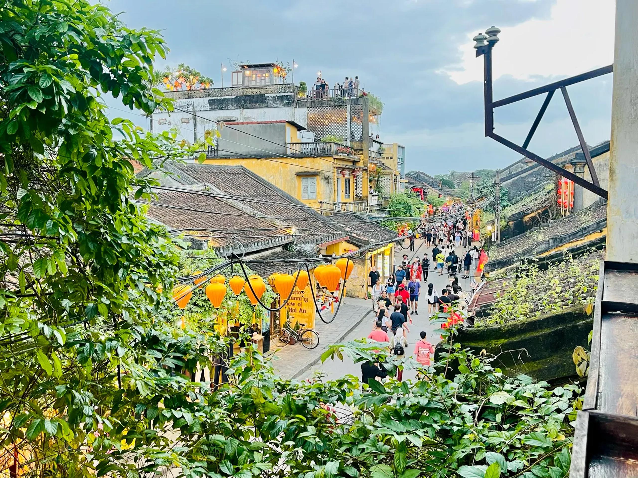 A Hoi An street seen from a rooftop, showing yellow buildings, tiled roofs and people walking below