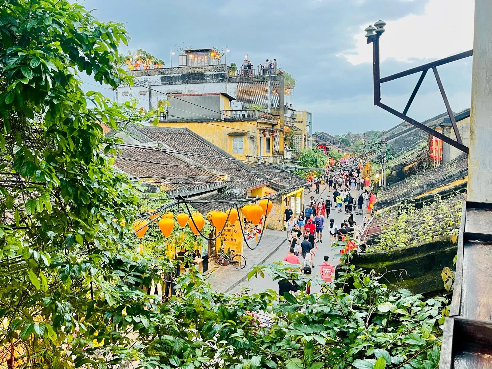 Hoi An Ancient Town seen from a rooftop, with tiled roofs, yellow walls and a street busy with people below