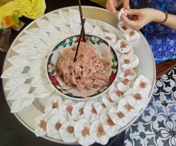 Hands pinching white rose dumplings around a bowl of shrimp filling